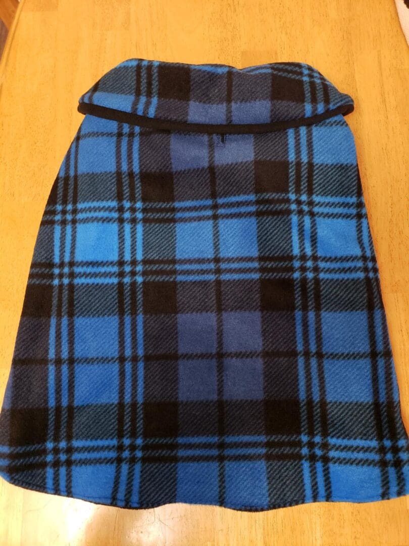 A blue and black plaid dog coat on the floor.