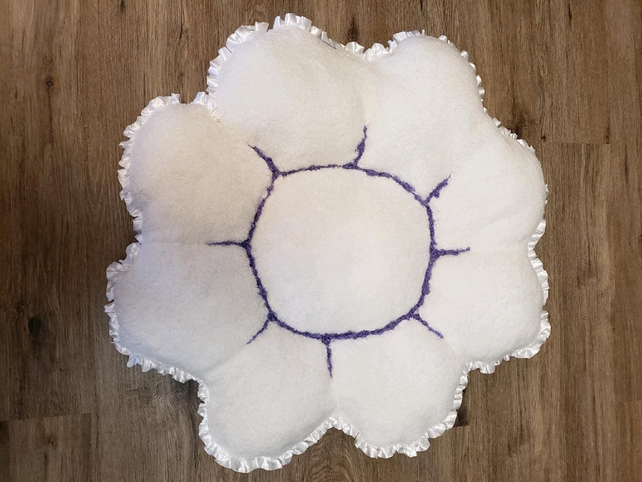 A white bowl with purple stitching on top of wooden table.