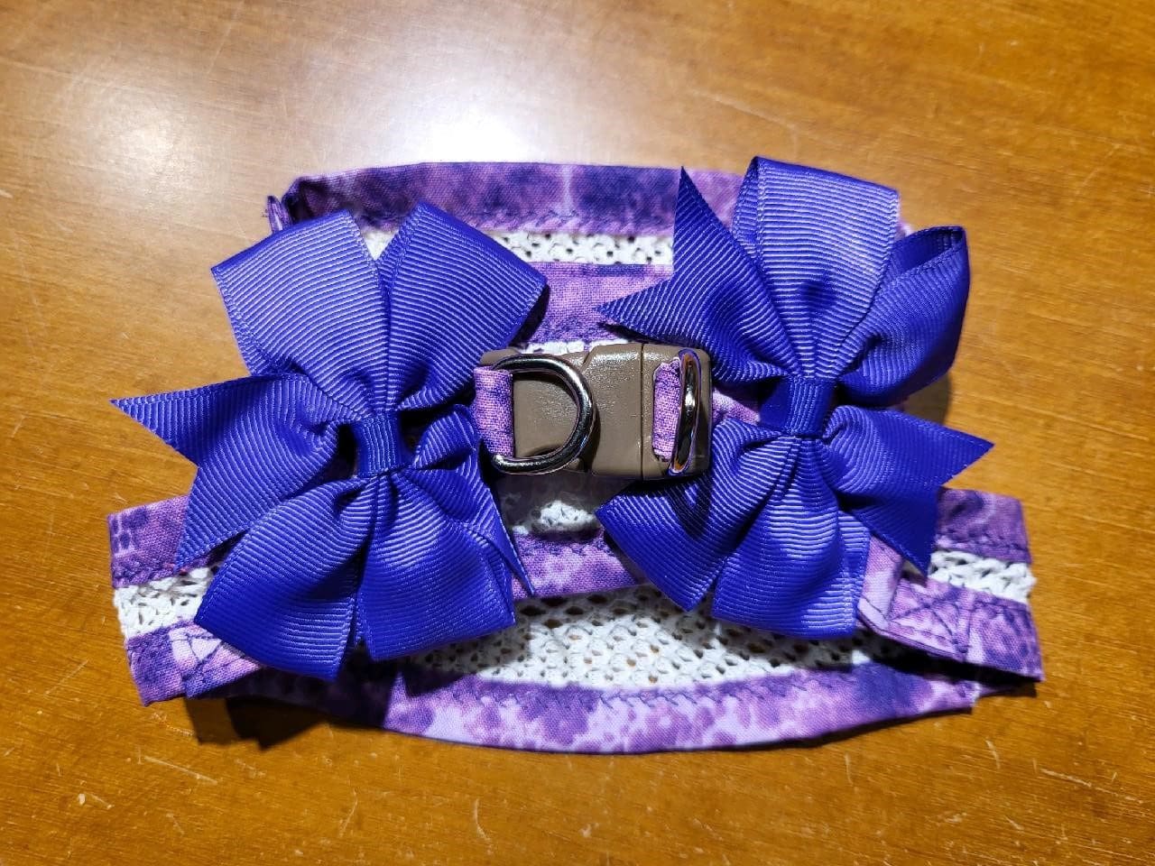 A purple dog collar with two bows on it.