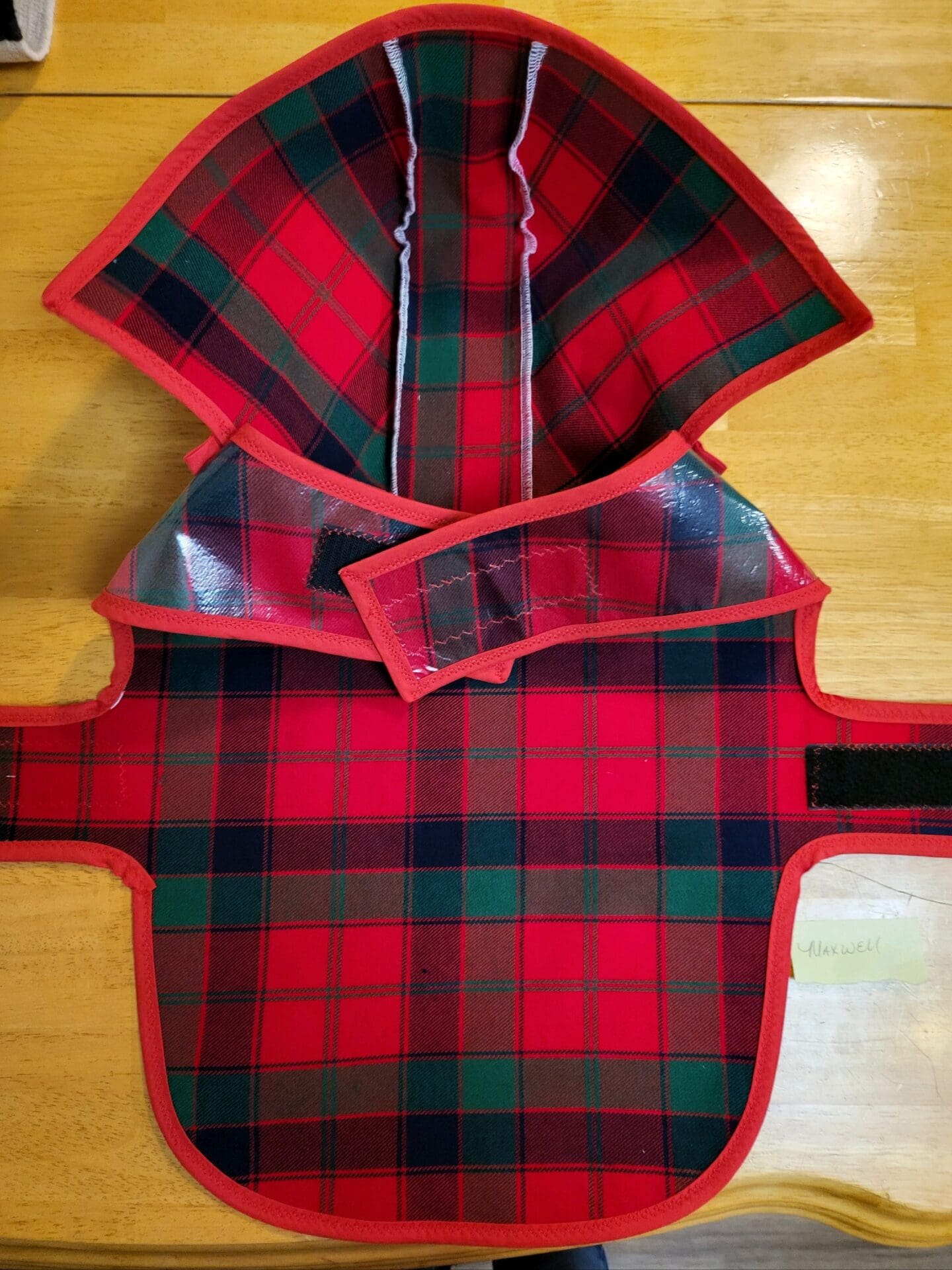 A red and black plaid dog coat on the floor.