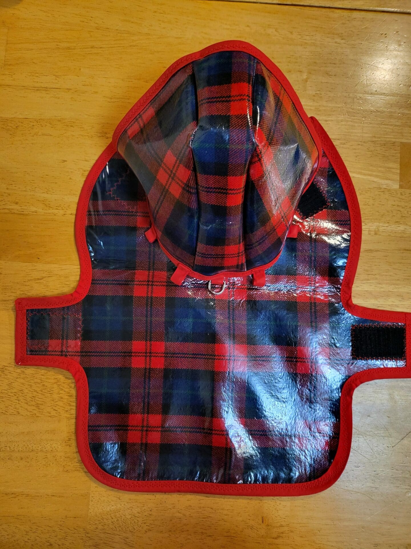 A red and black plaid dog coat on the floor.