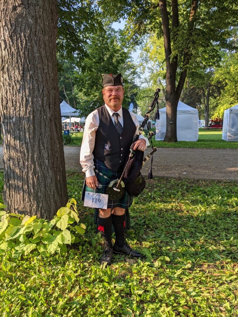 A man in kilt and vest holding a bagpipe.