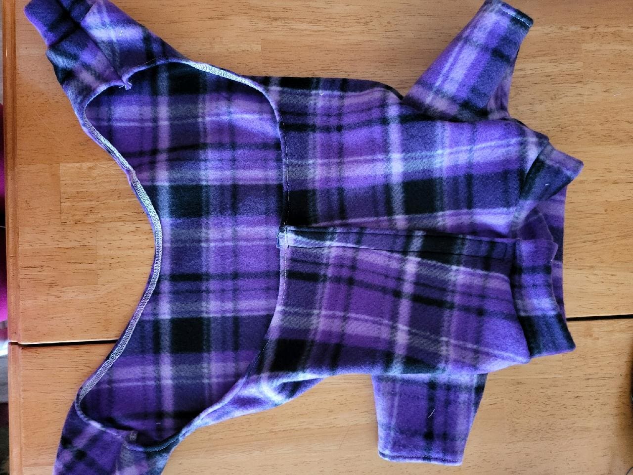 A purple plaid dog coat laying on top of a wooden table.