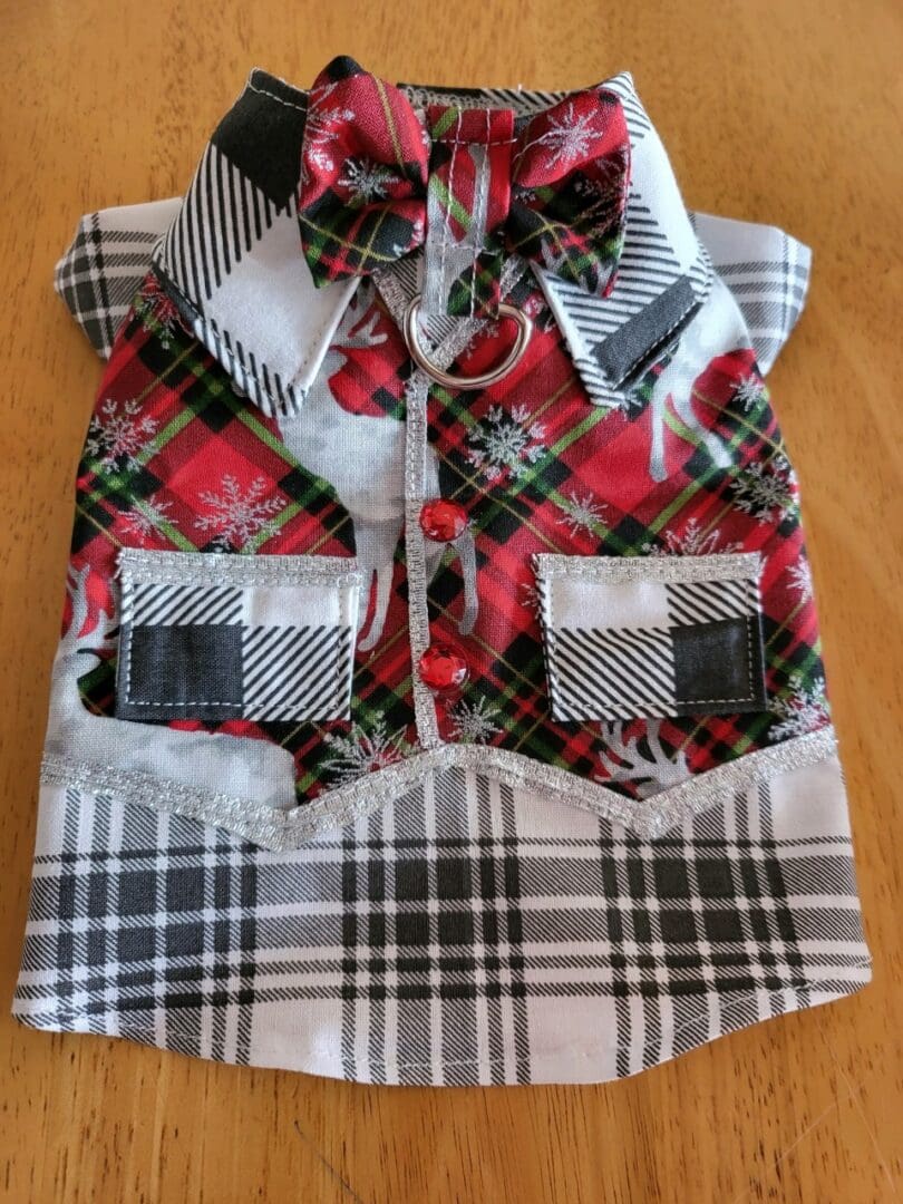 A dog 's shirt is decorated with plaid and has two pockets.