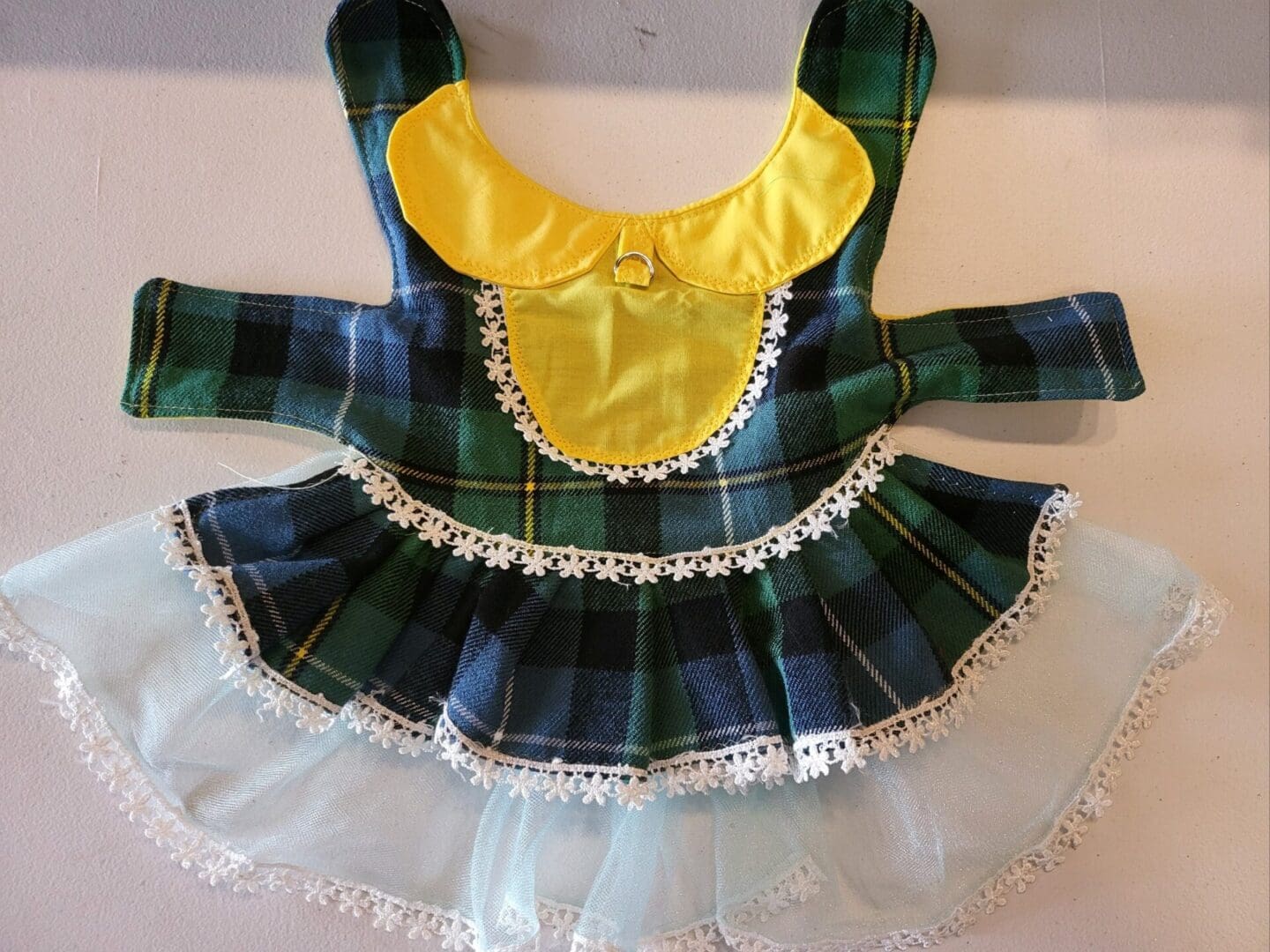 A green plaid dress with yellow trim and white ruffle.